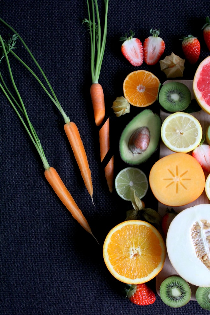 Vibrant assortment of cut fruit including grapefruit, lemon, kiwi, carrot, strawberry, avocado, and persimmon
